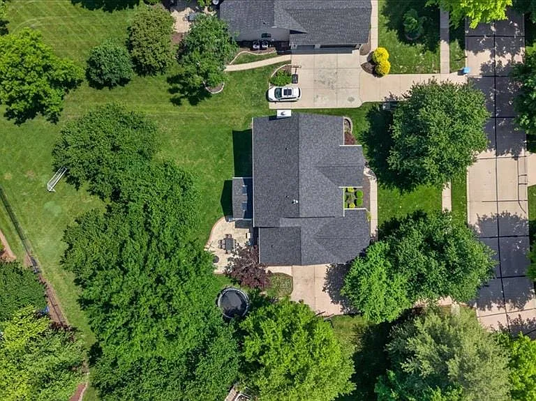 Expansive property featuring a dark-shingled roofline, multiple mature trees, a broad green lawn, and a paved driveway