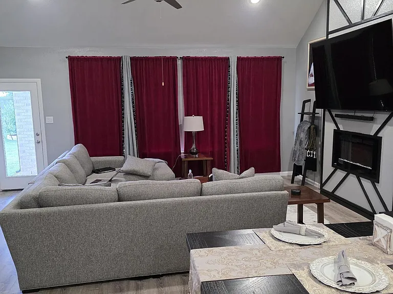 Open living area with sectional seating, ceiling fan, and an entertainment wall with fireplace, plus nearby dining space.
