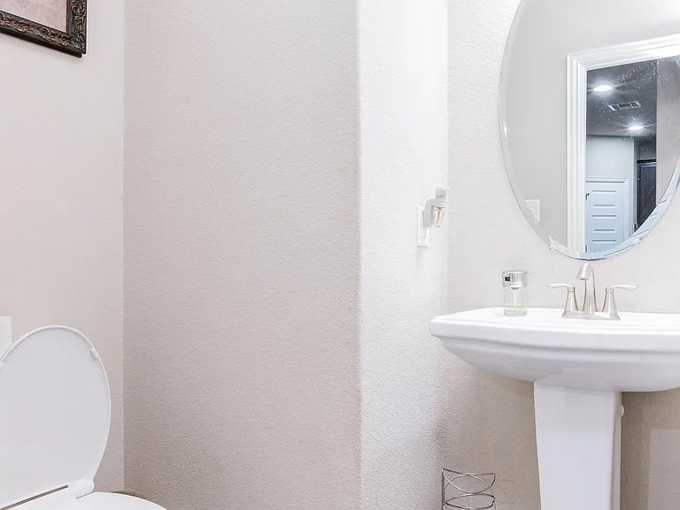 Bathroom with pedestal sink, round mirror, and standard toiletan easy-to-maintain space for daily routines.