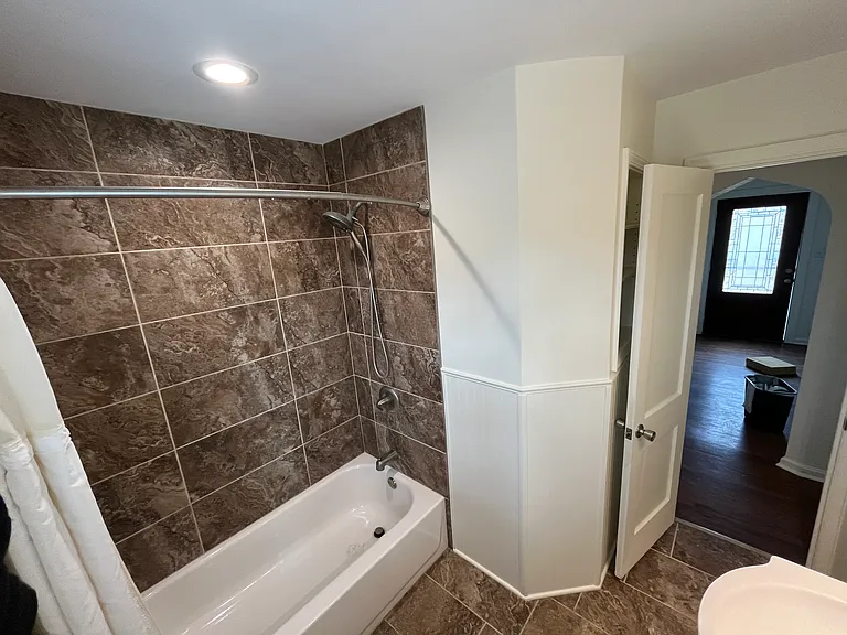 Shower/bath in main bathroom with shelving behind door.