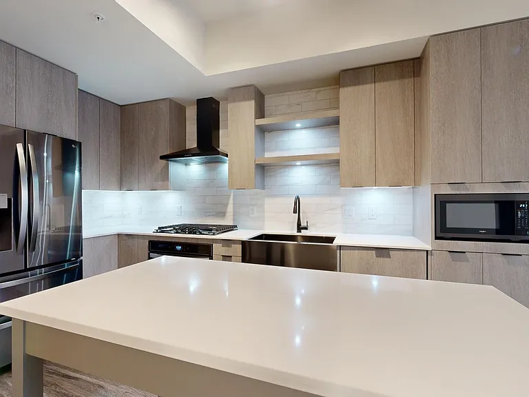 Apartment kitchen with black stainless steel appliances, quartz countertops, wood-style flooring, and custom Italian cabinetry.