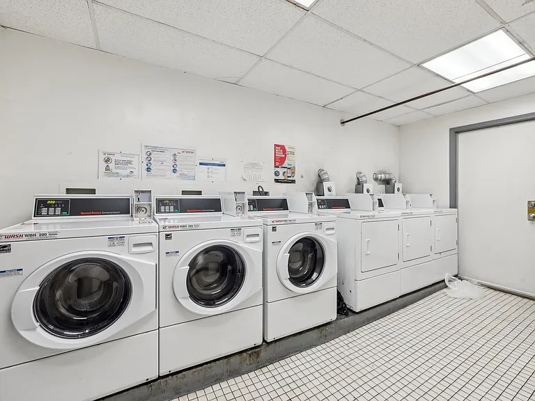 Laundry room with commercial washers and dryers, tiled floor, and posted instructions