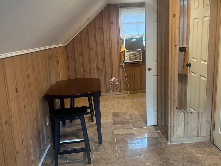 Compact dining nook with tile flooring, wood-paneled walls, and a window AC unit for added comfort.