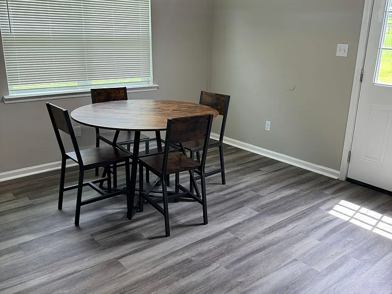 Dining nook with a round table set, overhead pendant lighting, and a large window for natural light near the exterior door.