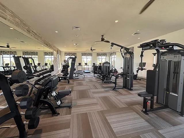 Spacious fitness center with cardio and strength equipment, mirrored wall, and large windows for an open feel.