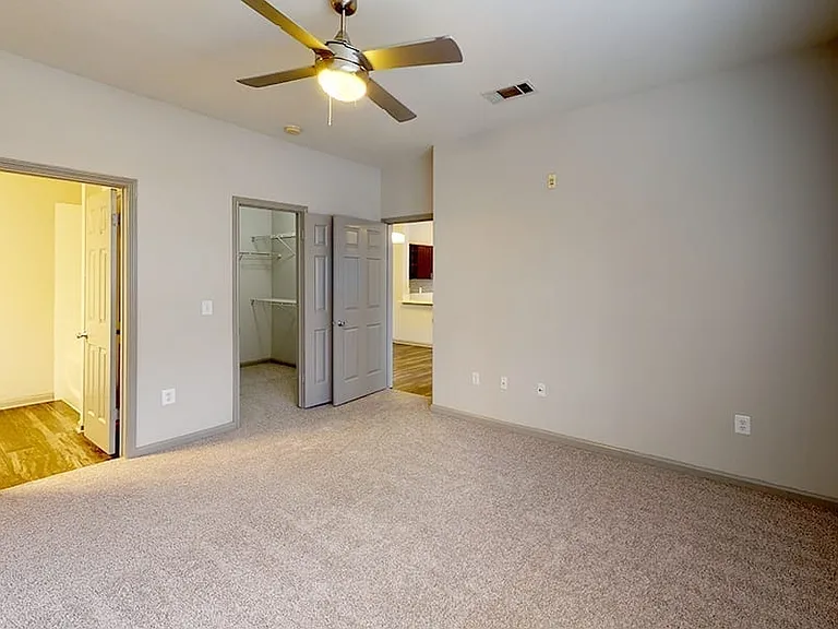 Spacious apartment bedroom with large closet, attached bathroom and plush carpet flooring.