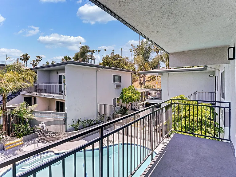 A second floor balcony with a pool view and trees.