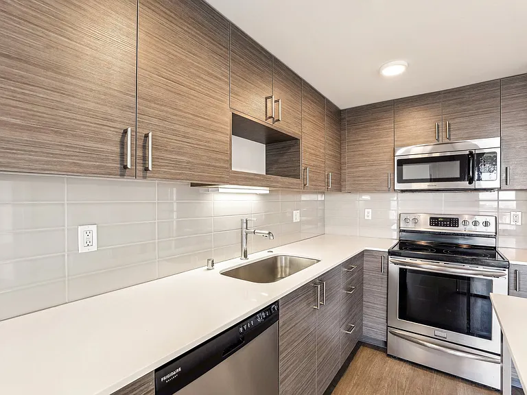 Contemporary kitchen with sleek wood-grain cabinetry, quartz countertops, and stainless steel Frigidaire appliances in a Seattle, WA apartment. Ideal for urb...