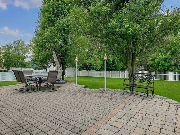 Charming Outdoor Brick Paver Patio with Light Posts Overlooks Large Fenced in Yard.