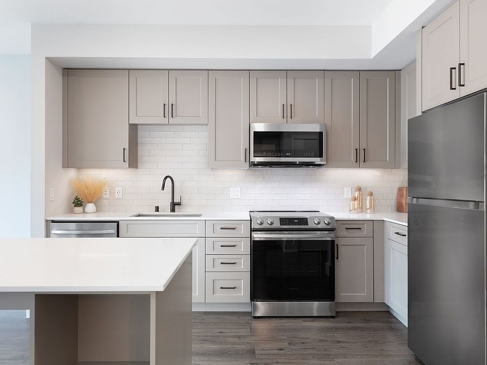 Coming Soon - New West Phase apartments - Finish Package III Kitchen with stainless steel appliances, white quartz countertops, grey cabinetry, pendant lighting, and hard surface flooring (Representative photo)