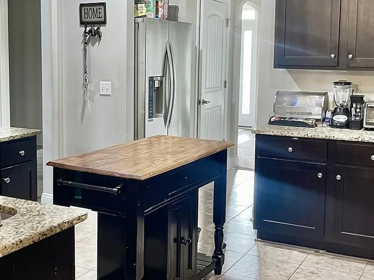 Spacious kitchen with granite counters, dark cabinetry, stainless refrigerator, and a movable prep island for added workspace