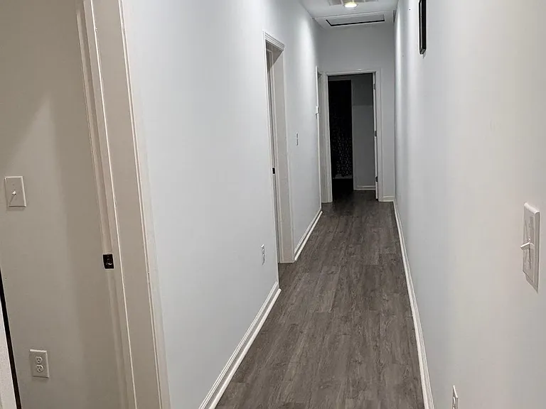 Long hallway with durable wood-look flooring, recessed lighting, and multiple doorways providing access to bedrooms and baths