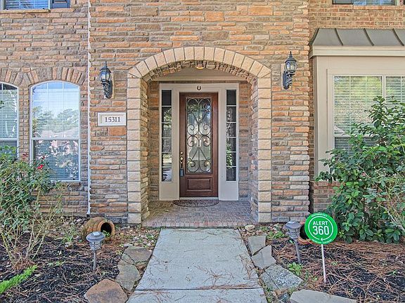 This lovely brick and stone entry features a wrought iron and glass front door with brick flooring.