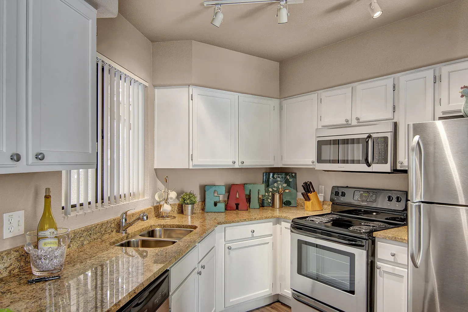 Kitchen with white cabinets, granite countertops, stainless steel appliances including a refrigerator, oven, and microwave.