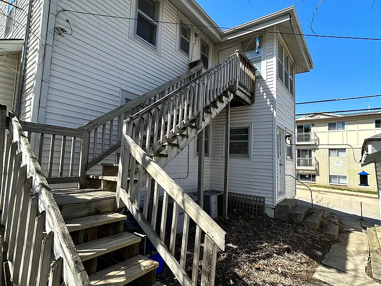 Rear of home with exterior entrance. At the bottom of the stairs is a small outdoor fire pit or sitting area. The walkway on the right side will lead to the covered off-street parking.