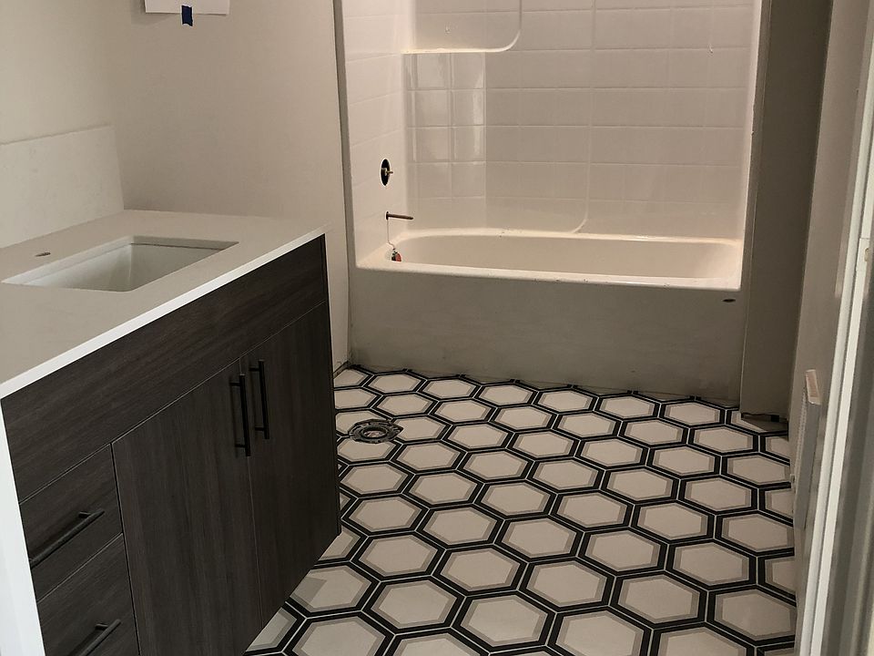 Each bathroom vanity has a bank of drawers in addition to sink cabinet for extra storage. Matte black hardware. Floor tiled with a shower/tub surround.