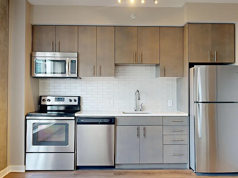 Apartment kitchen with stainless steel appliances, quartz countertops and wood-style flooring.