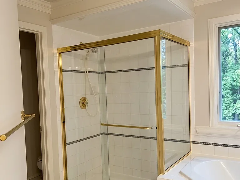 eparate glass-enclosed shower featuring elegant brass trim, a spacious interior with custom tile work, and a decorative accent band.