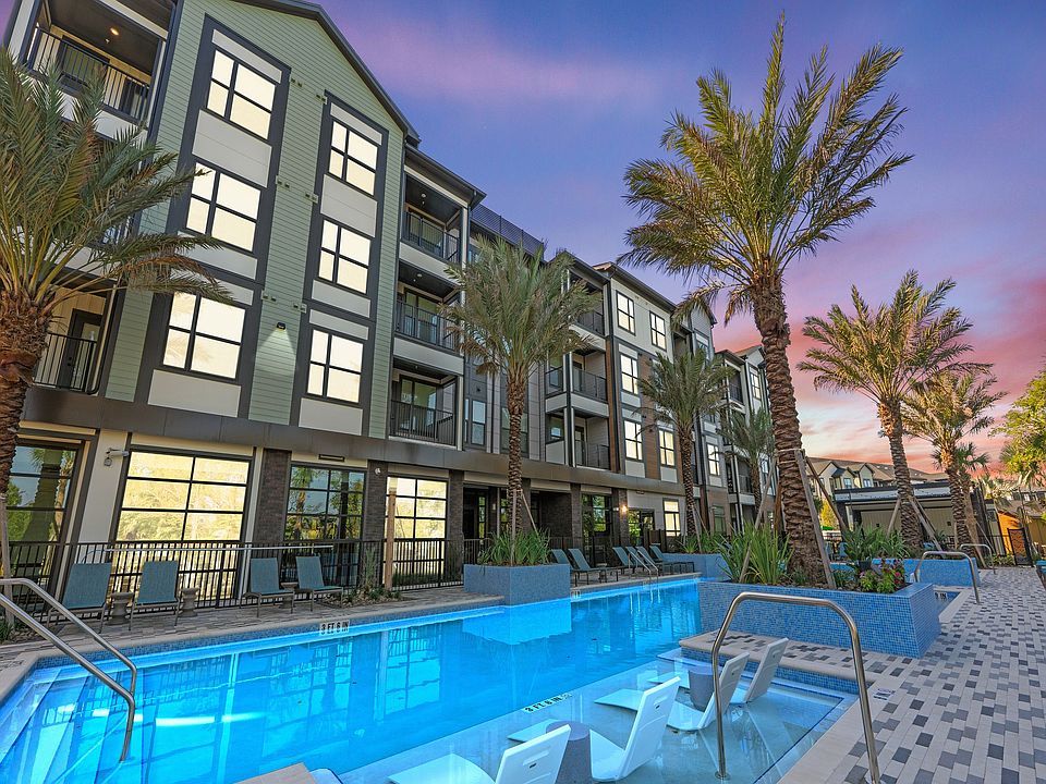 Modern apartment building with stylish balconies overlooking a luxurious pool and palm trees under a vibrant sunset sky.