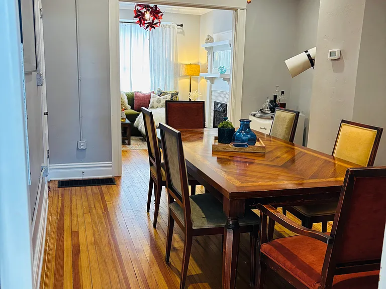 A sleek wine fridge offers a modern touch for wine enthusiasts. The room is illuminated by a striking, contemporary chandelier, perfectly balancing vintage charm with modern flair. Natural light streams from the living room for a soft, inviting glow.