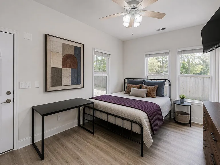 Private bedroom with two windows, ceiling fan, wall-mounted TV, and space for a desk and dresser.