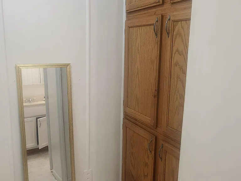 Hallway nook with floor-to-ceiling wood cabinets and tiled flooring, offering convenient built-in storage near the bath.