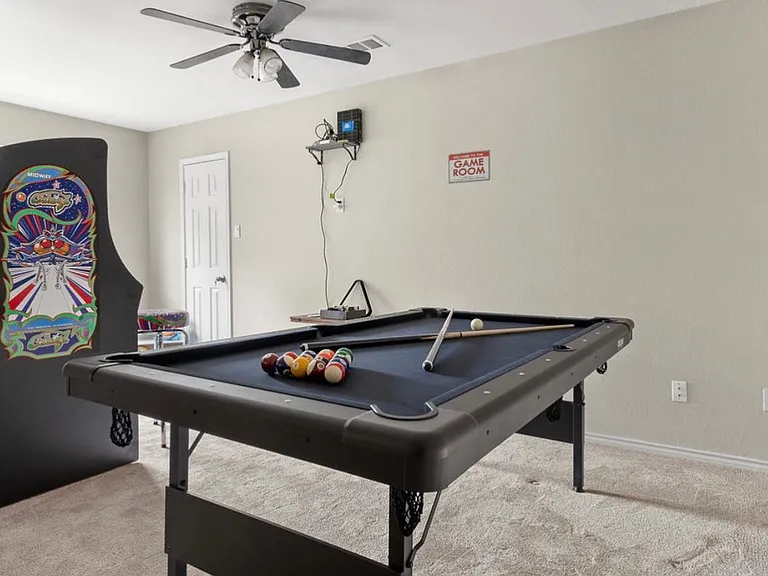 Gameroom features a pool table, an arcade, and an area for children to sit and read or play which features a desk with a chair, a bookcase with books and toys.