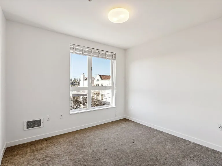 Spacious unfurnished bedroom at 4400 Alaska in Seattle, WA, featuring bright natural light from a large window and plush carpet, perfect for your personal re...