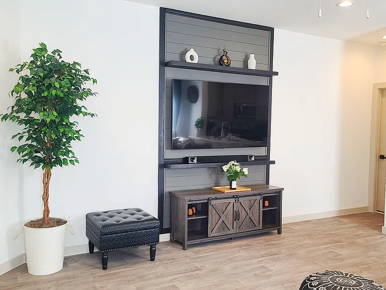 Open living area with wood-look flooring and a built-in media wall featuring a large TV and storage console.