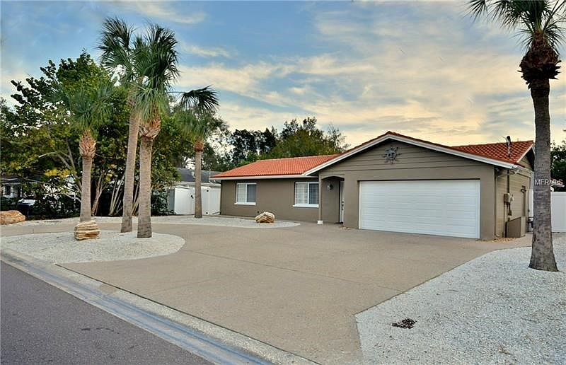 Front of the home with circular driveway, lots of palm trees, decorative stones and xeriscape landscaping.