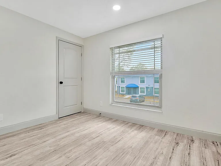 Bright and modern bedroom with sleek flooring, ample natural light, and a view of the charming neighborhood from the window.