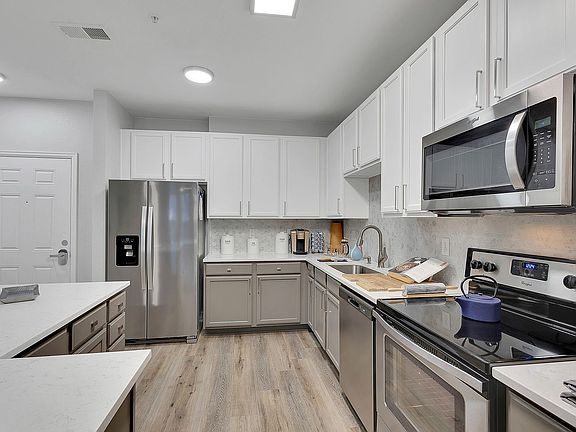 Modern kitchen with sleek stainless steel appliances, elegant white cabinetry, and stylish wood flooring, perfect for culinary enthusiasts.