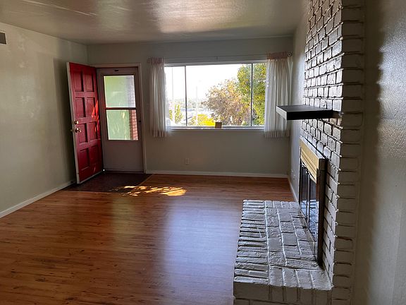 View of the entrance into the living room, with the fireplace. The large front window shows the front garden and a wide-open sky.