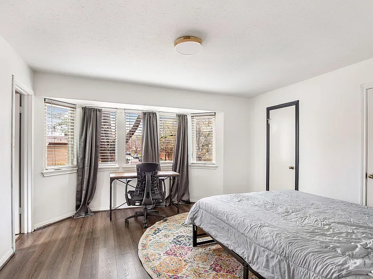 Spacious bedroom with wide windows, wood-style floors, plus a dedicated desk/work area.