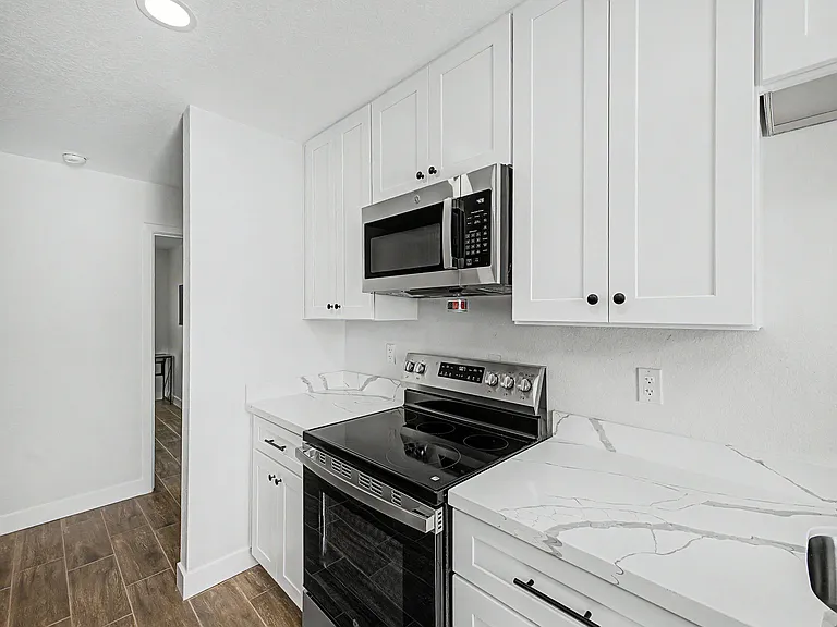 Kitchen features ample white cabinetry, marble-look counters, and a smooth-top range with an over-the-range microwave.