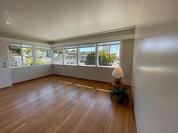 Look at the newly refinished hardwood floor in this light-filled living room. The front door on left is entrance to your apartment. Feels more like a house. The windows welcoming in lots of light make this a bright space to call home.