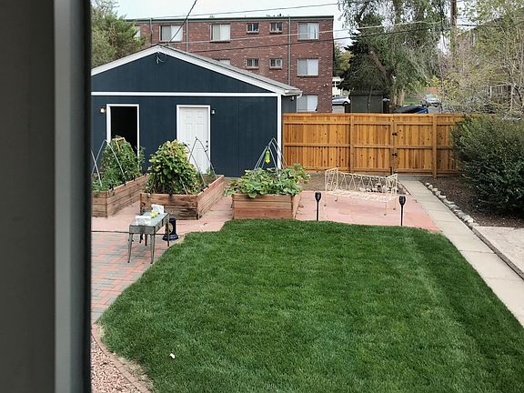 View from kitchen window into enclosed backyard with garden boxes and newly built garage. Offsite outdoor parking space is on the other side of wooden fence, in addition to one garage space.