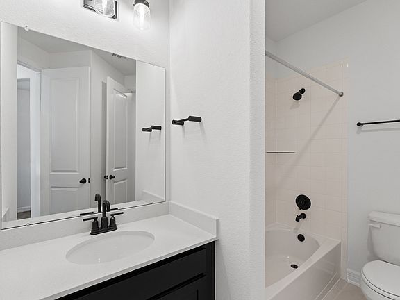 The secondary bath features tile flooring, dark stained cabinetry and light countertops and a shower