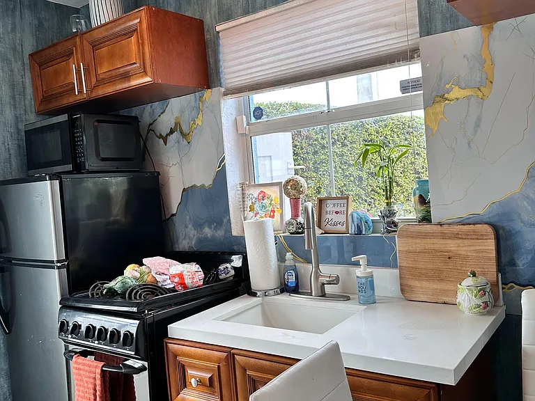 Compact kitchen with a full-size range, microwave, stainless refrigerator, and sink set beneath a window for easy meal prep.