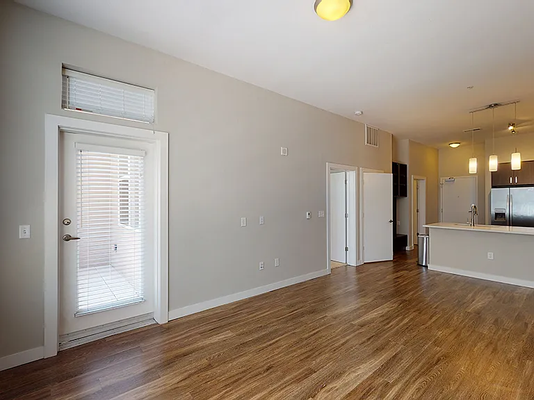 Apartment kitchen with stainless steel appliances, dining and living room with wood-style flooring.