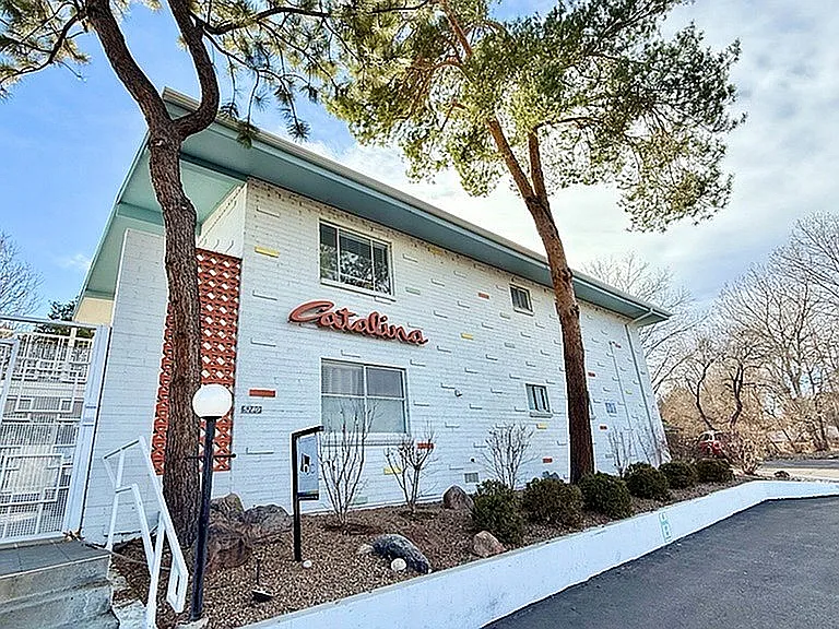 Charming white apartment building with unique exterior, surrounded by lush greenery and a spacious driveway.