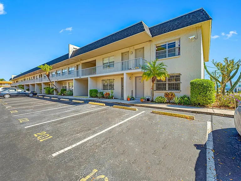 Charming two-story apartment building with lush palm trees and ample parking, bathed in bright natural light.