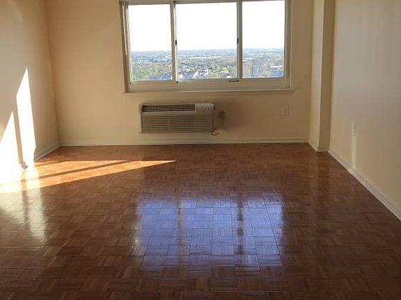 Living room with lustrous parquet wood flooring and oversized window with spectacular view of Rutgers campus, Raritan river and Manhattan skyline