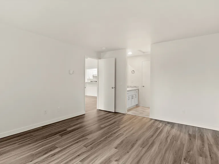 Bright, spacious room with elegant wood flooring leading to a modern kitchen and bathroom area. Bright, spacious room with elegant wood flooring leading to a modern kitchen and bathroom area.