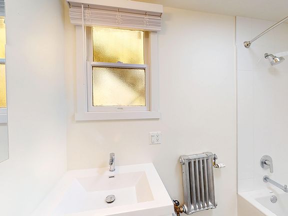 Bathroom with a sink, chrome faucet, and a shower area , frosted windows and a vintage radiator add character