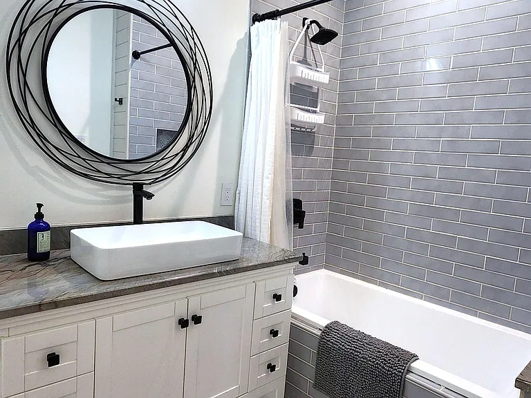 Updated bathroom with a tiled tub/shower, wide vanity with ample storage, and modern lighting with a statement mirror.