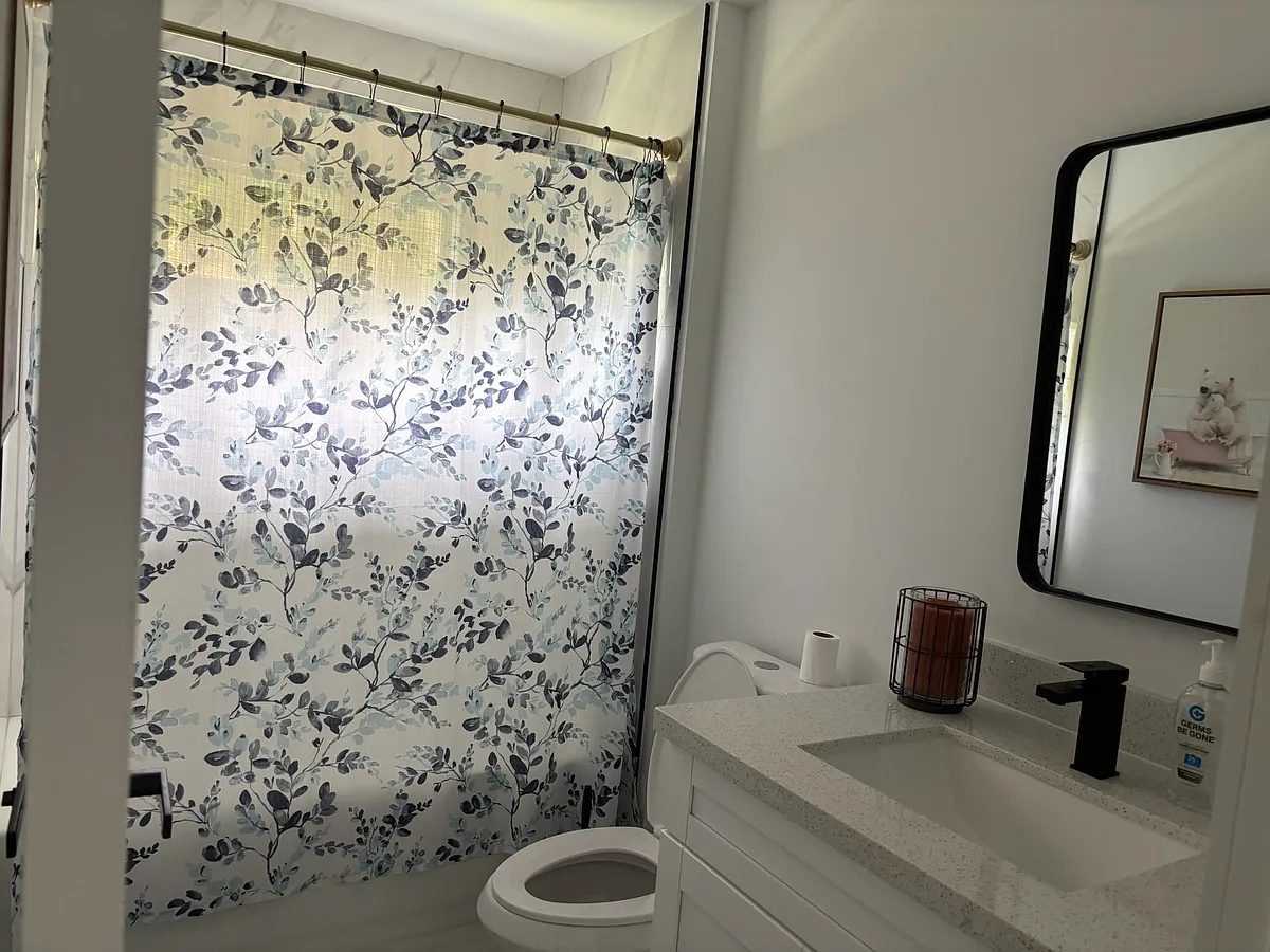 Clean full bathroom with a shower/tub combo, floral curtain, and a wide vanity countertop with modern fixtures. - NW 27th Pl