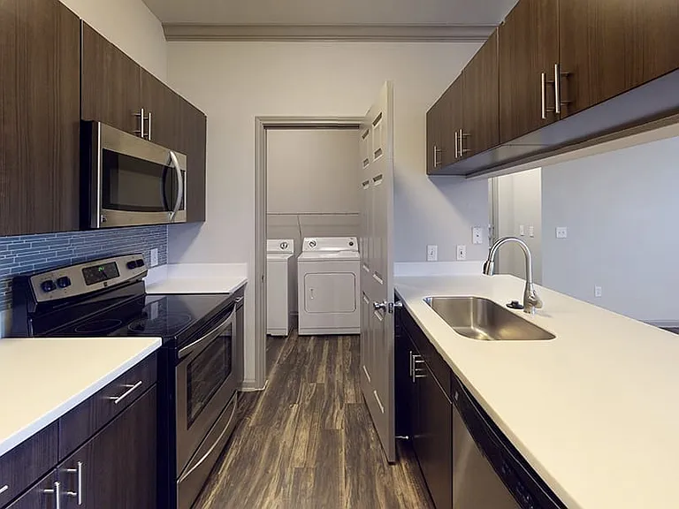 Apartment kitchen with stainless steel appliances, quartz countertops and wood-style flooring.
