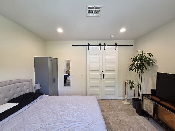 Furnished bedroom with queen bed, desk, high ceilings.