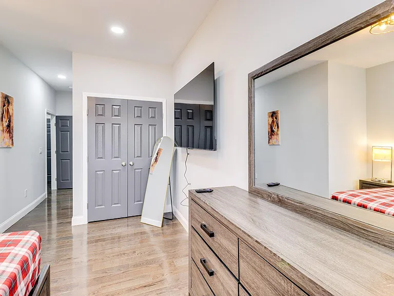 Furnished bedroom with hardwood floors, double-door closet storage, and a dresser with mirror plus wall-mounted TV.